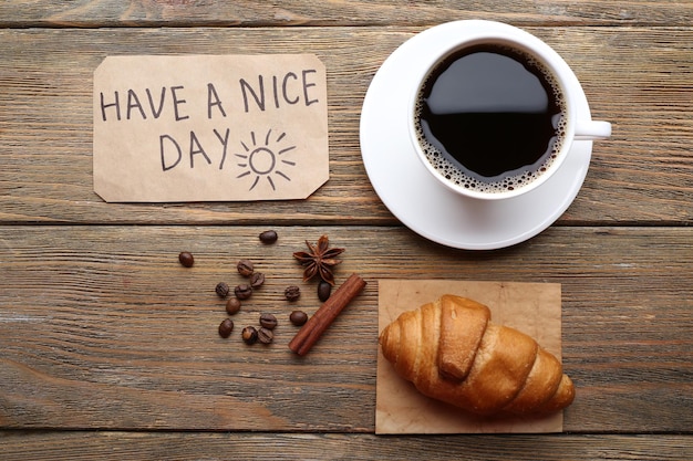 Cup of coffee with fresh croissant and Have A Nice Day massage on wooden table top view