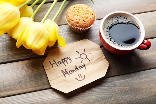 Cup of coffee with fresh cupcake tulips and Happy Monday massage on wooden background