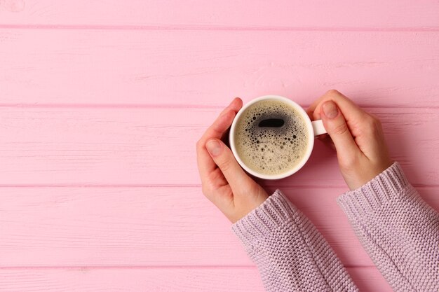 Tazza di caffè con schiumoso in mani femminili sulla vista del piano del tavolo in legno