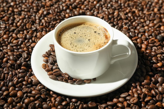 Cup of coffee with frothy foam on beans background