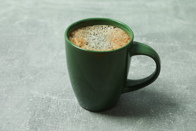 Tazza di caffè con schiuma schiumosa e chicchi di caffè su sfondo grigio