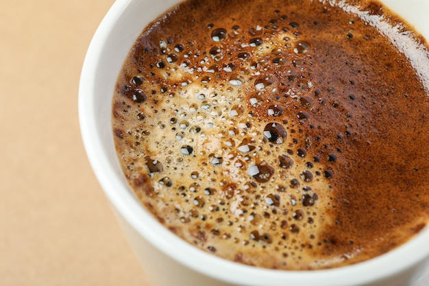 Cup of coffee with frothy foam on light background