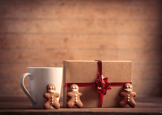 Cup of coffee with gingerbread man and Christmas gift on wooden table