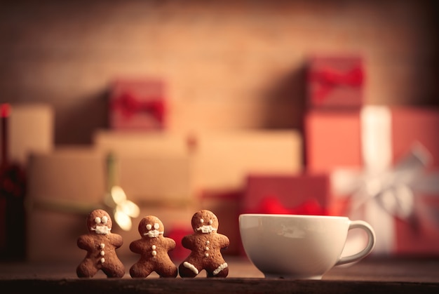 Cup of coffee with gingerbread man and Christmas gift on wooden table