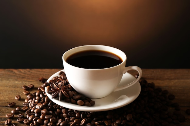 Cup of coffee with grains on wooden table on dark