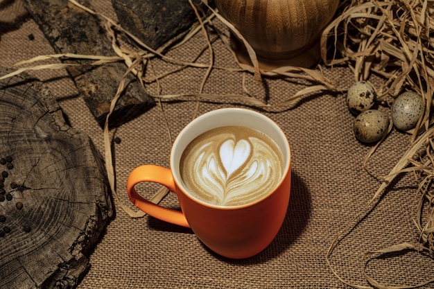 나무 배경에 흰색 컵에 심장 패턴으로 커피 한 잔.