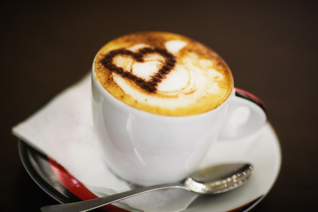 나무에 흰색 컵에 하트 패턴으로 커피 한 잔