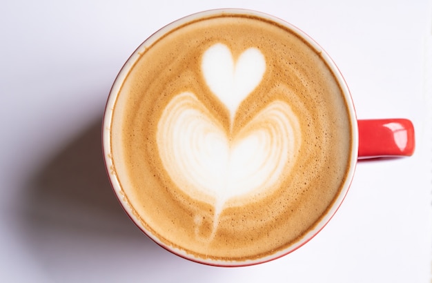 La tazza di caffè con una bolla a forma di cuore riposa su una priorità bassa bianca.