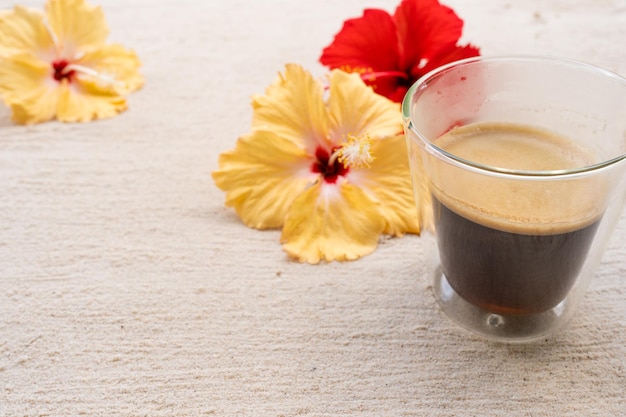 Cup Coffee with hibiscus on sand beach.