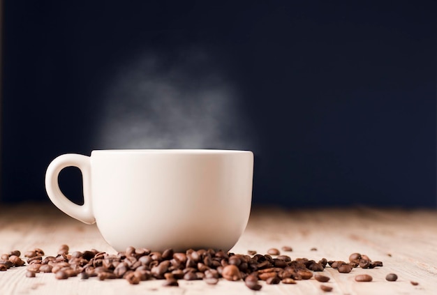 cup of coffee with hot steam roasted coffee beans on wooden table with blue background