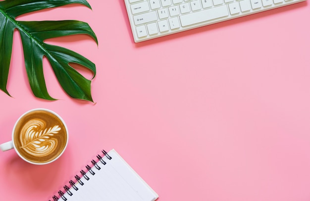 A cup of coffee with keyboard and copy space on pink background. Office desk and drink concept.