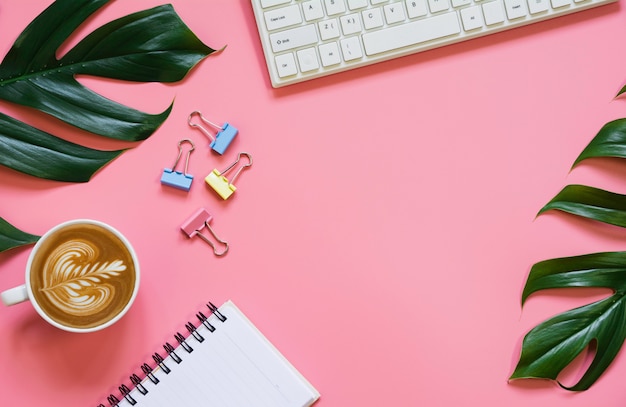 A cup of coffee with keyboard and copy space on pink\
background. office desk and drink concept.