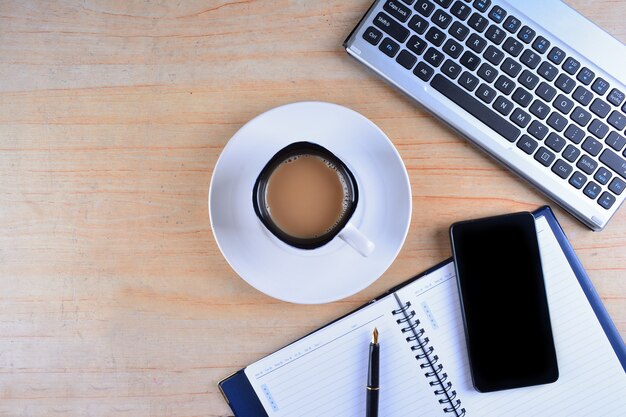 Cup of Coffee with keyboard and mouse, fountain pen, notebook, calculator and smartphone on a table