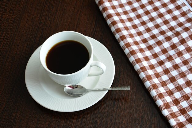 cup of coffee with kitchen tablecloth on wooden table background