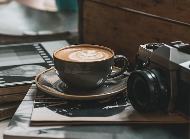 Photo cup of coffee with latte art on books next to vintage film camera