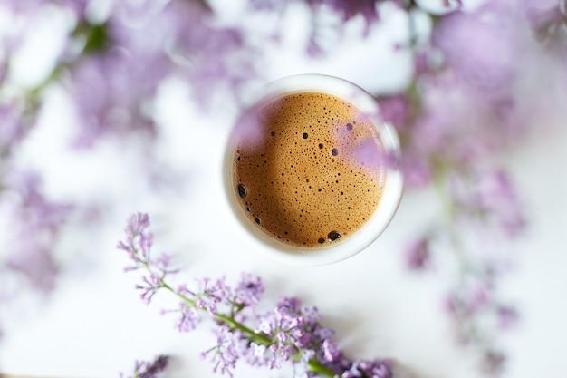 Cup of coffee with lilac petals, cup of coffee near bouquet of spring flowers on white background. morning inspiration