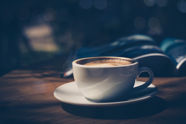 cup of coffee with magazine on table in cafe in dark tone and vintage 