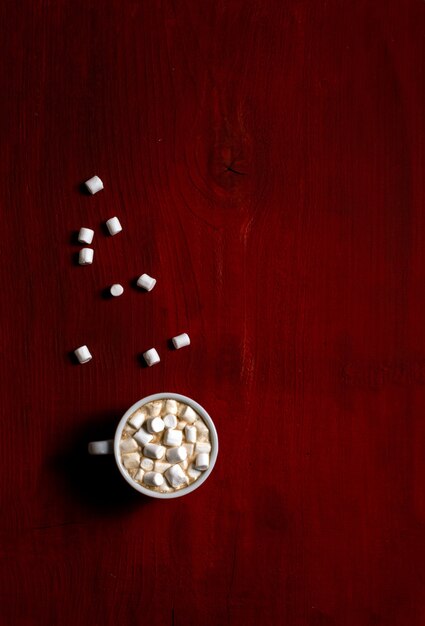 Cup of coffee with marshmallow on red wooden background