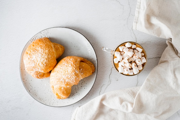 Cup of coffee with marshmallows and croissants on a plate on the table Homemade breakfast lifestyle Top view