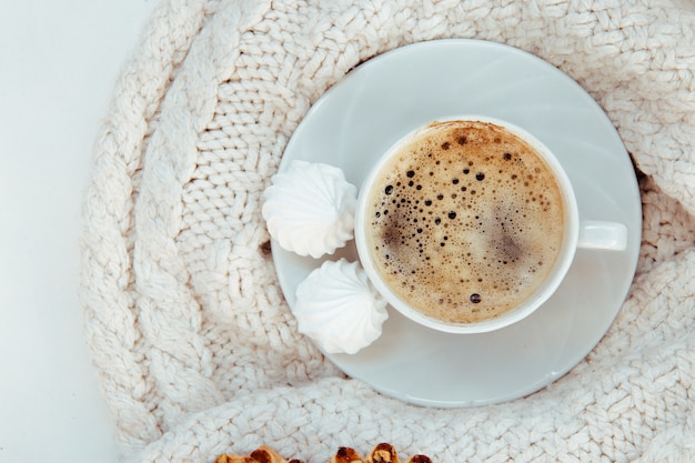 Cup of coffee with meringues and knitted sweater - top view.