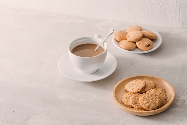 明るい石の背景にミルクまたはクッキーとカプチーノとコーヒーのカップ