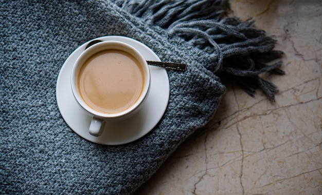 Cup of coffee with milk on cozy knitted winter blanket