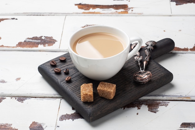 A Cup of coffee with milk and cubes of cane sugar on a wooden table