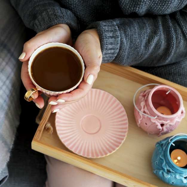 A cup of coffee with milk in female hands on a wooden tray