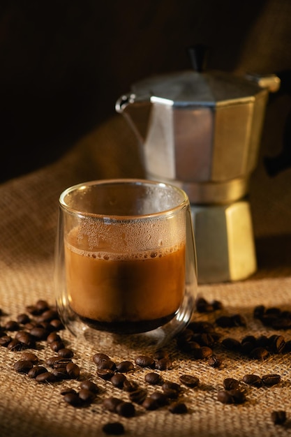 Una tazza di caffè con latte e una caffettiera geyser su uno sfondo di tela scura