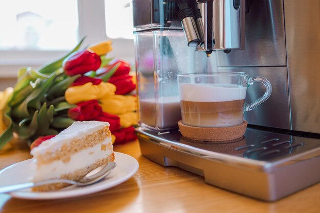木製のキッチンテーブルに淹れたてのミルクケーキとチューリップの花を入れたコーヒーカップ
