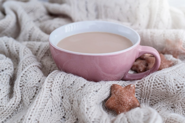 Cup of coffee with milk and star shaped ginger cookies on warm knitted beige blanket.