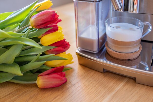 Cup of coffee with milk and tulips flowers on wooden kitchen table freshly brewed cappuccino