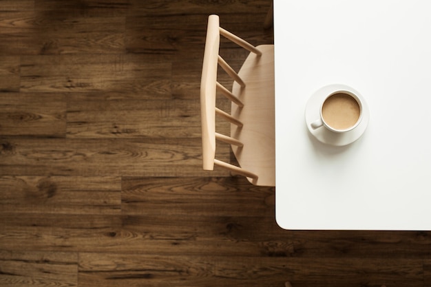 Cup of coffee with milk on white table near designer chair and wooden floor