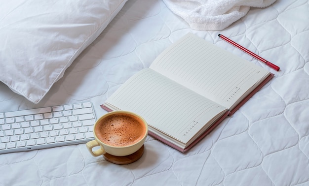 Cup of coffee with notebook and keyboard on the bed