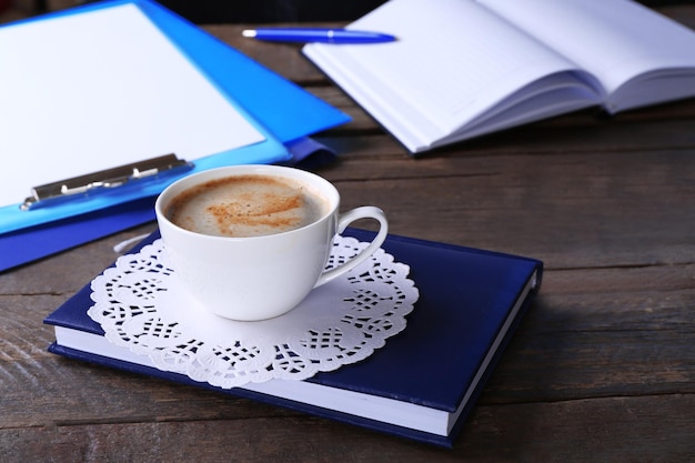 Cup of coffee with notebooks and clipboard on wooden table closeup