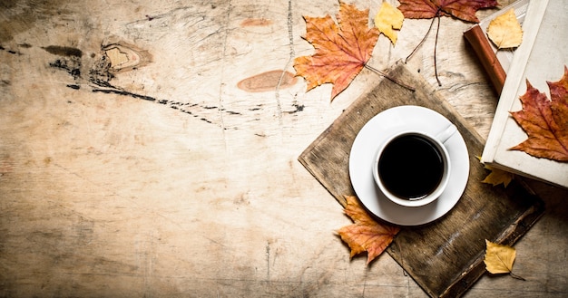 Cup of coffee with an old book and maple leaves. On wooden background.