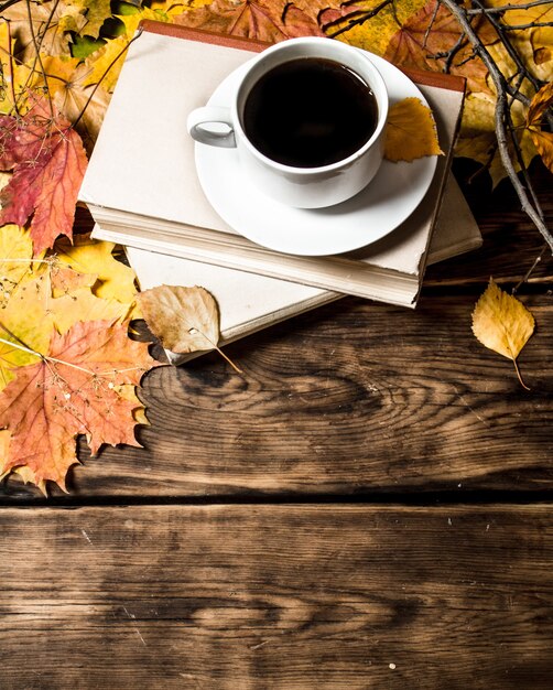 Cup of coffee with an old book and maple leaves on wooden background