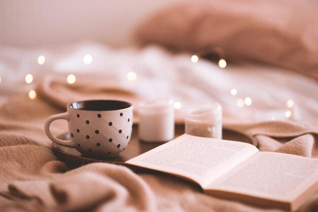 Cup of coffee with open book and candles in bed closeup. Autumn season. Good morning. Selective focus.