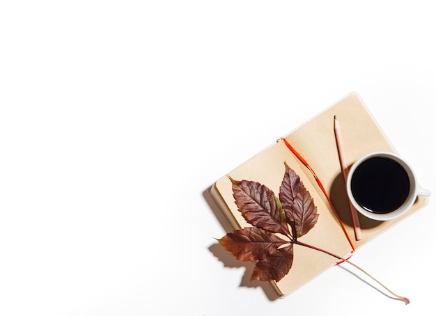 Cup of coffee with open notepad and chestnut leaves isolated on white background