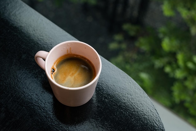 A cup of coffee with a pink handle sits on a ledge.