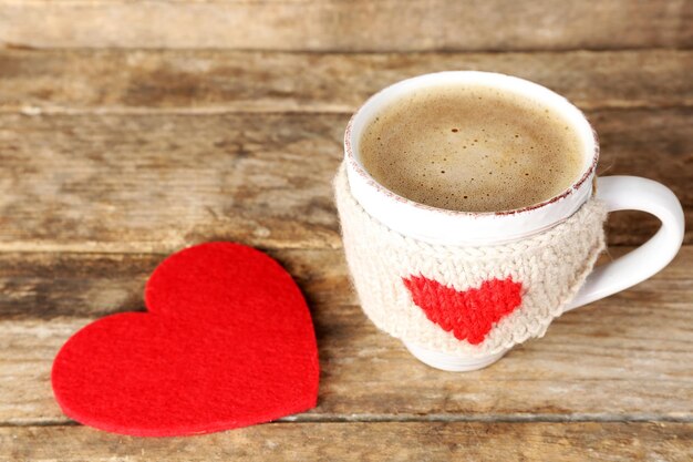 Cup of coffee with red felt hearts on wooden background, close up