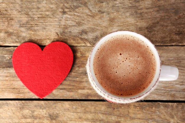 木製のテーブルに赤いフェルトの心とコーヒーのカップ、クローズアップ