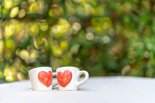 Tazza di caffè con cuore rosso stampato sulla sabbia su sfondo bokeh di natura.