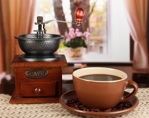 Cup of coffee with scarf and coffee mill on table in room