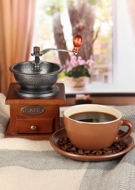 Cup of coffee with scarf and coffee mill on table in room