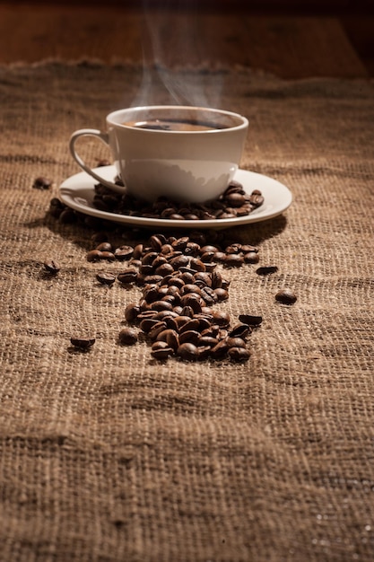 Cup of coffee with smoke and coffee beans on burlap on old wooden background