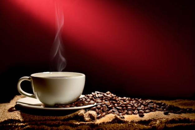 Cup of coffee with smoke and coffee beans on reddish brown background