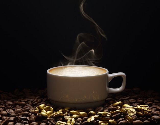 暗い背景に黄金のコーヒー豆の煙とコーヒーのカップ