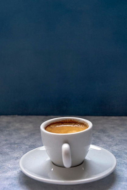 Cup of coffee with spoon on a white textured surface in front of a blue background. It has negative