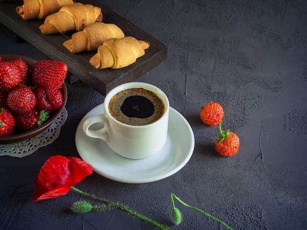 cup of coffee with strawberries and croissants on a wooden tray